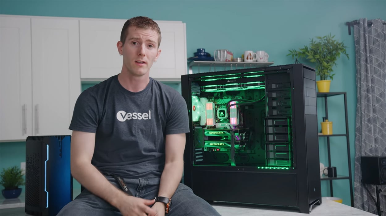 Linus Sebastian of Linus Tech Tips sat on a desk next to a PC inside an E-ATX case.